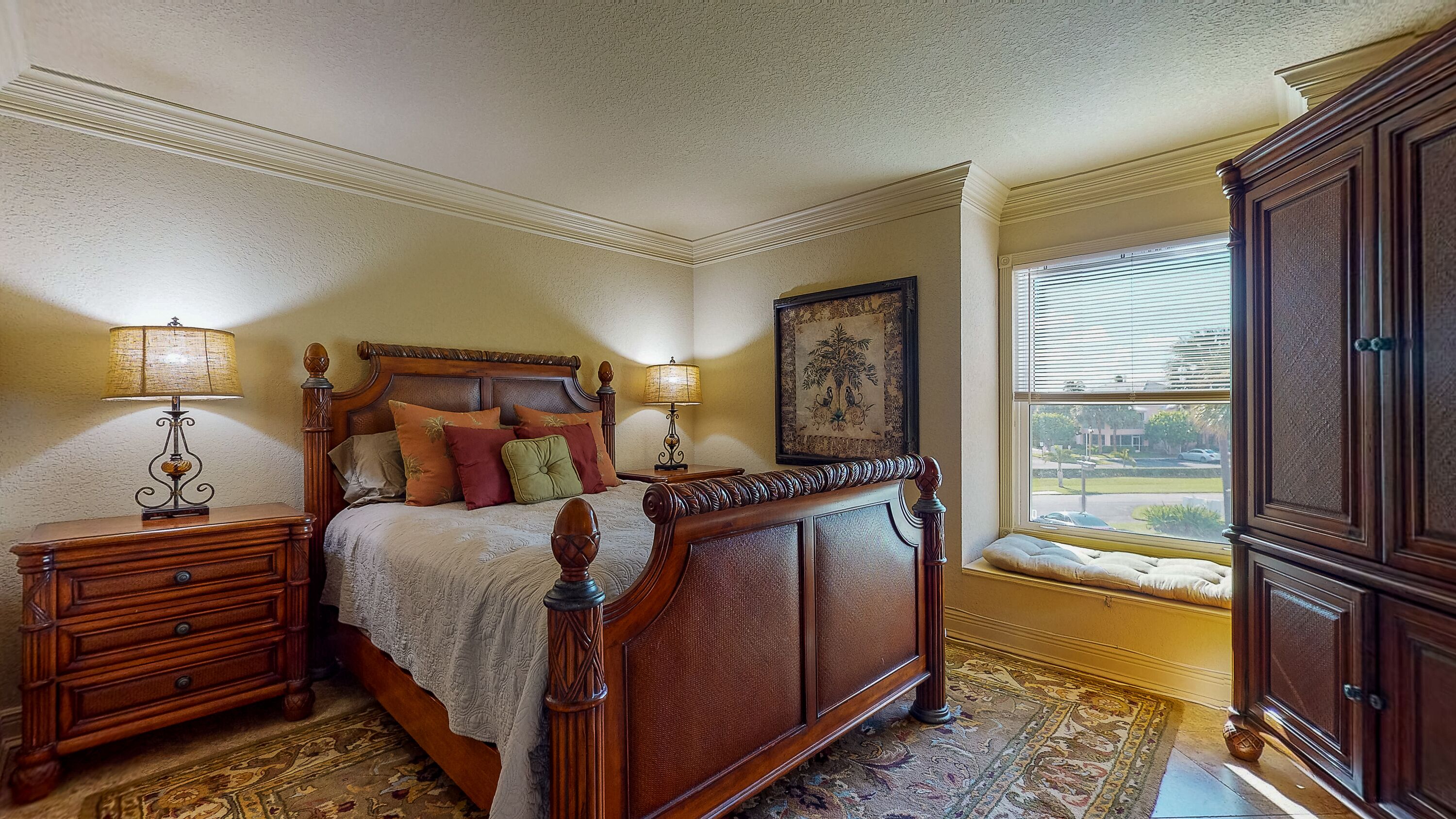 Un dormitorio con una cama de madera grande, dos mesitas de noche con lámparas, un cuadro enmarcado en la pared y una ventana con vistas al exterior.