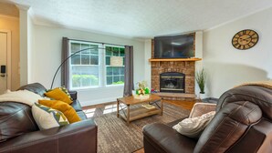 A living room with leather sofas, a fireplace, a flat-screen TV, and a large window with curtains. - Heated Private Saltwater Pool; Hot Tub; 15 min AVL; 10 min Blue Ridge Parkway (Candler)