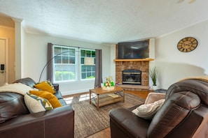 A living room with leather sofas, a fireplace, a flat-screen TV, and a large window with curtains. - Heated Private Saltwater Pool; Hot Tub; 15 min AVL; 10 min Blue Ridge Parkway (Candler)