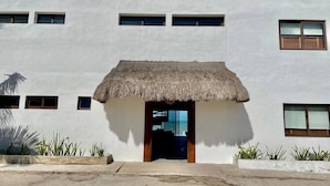 A white building with a thatched-roof entrance and multiple windows. - Casa A LA Orilla DEL MAR CON Piscina (Telchac Puerto)
