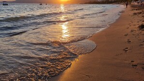 Una spiaggia al tramonto, con onde e una montagna in lontananza.