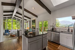 A spacious kitchen with a large island, dark wooden floors, and a view of greenery through large windows.