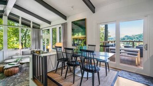 A modern dining area with a glass table and chairs, a sofa, and a view of the outdoors. - Mid-century home with panoramic views and hot tub! (Maggie Valley)