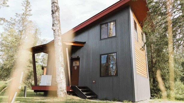Un edificio moderno de dos pisos con techo inclinado, ventanas grandes y una terraza de madera.