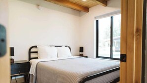 Un dormitorio con una cama, una mesita de noche, una ventana y techo de madera.