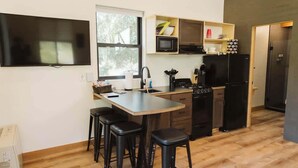 Una cocina compacta con una televisión de pantalla plana, microondas, refrigerador y cafetera. Hay tres taburetes y una pequeña isla con un lavamanos.