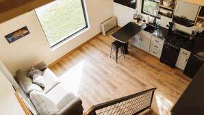 A compact kitchen with a dining area, a ceiling fan, and a large window providing natural light. - Lynx Cabin @ Keystone Kozy (Soldotna)