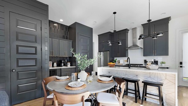 Una cocina moderna con armarios oscuros, una isla central y una zona de comedor con sillas de madera y una mesa redonda.