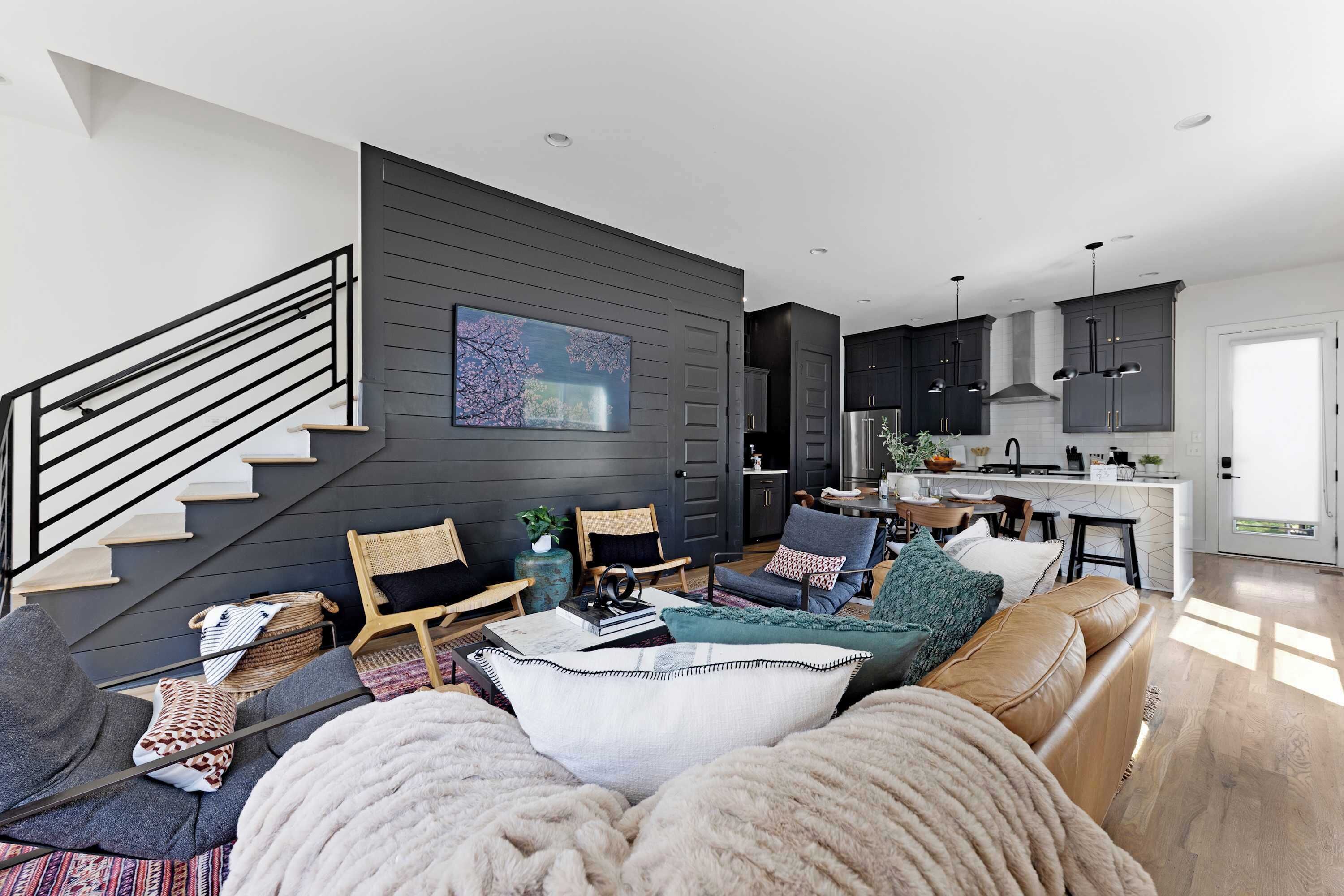 Una sala de estar moderna con una escalera, un conjunto de sofás y una zona de cocina.
