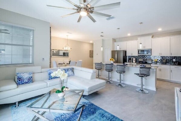 A modern living room with a white sofa, a glass coffee table, and a ceiling fan.