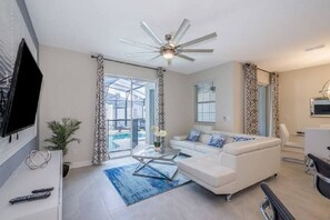 A modern living room with a white sofa, a glass coffee table, and a ceiling fan.