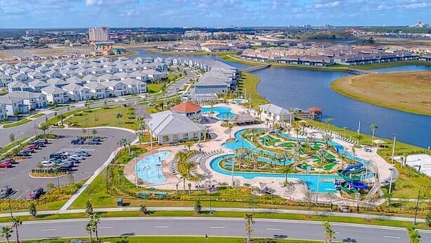 Un quartier résidentiel doté d’une grande piscine, d’un port de plaisance et d’une rue bordée de voitures garées.