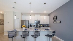 Une cuisine moderne avec des meubles blancs, un îlot central doté de tabourets et des luminaires suspendus.