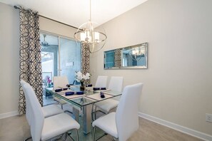 A dining area with a glass table, white chairs, a chandelier, and a mirror on the wall.