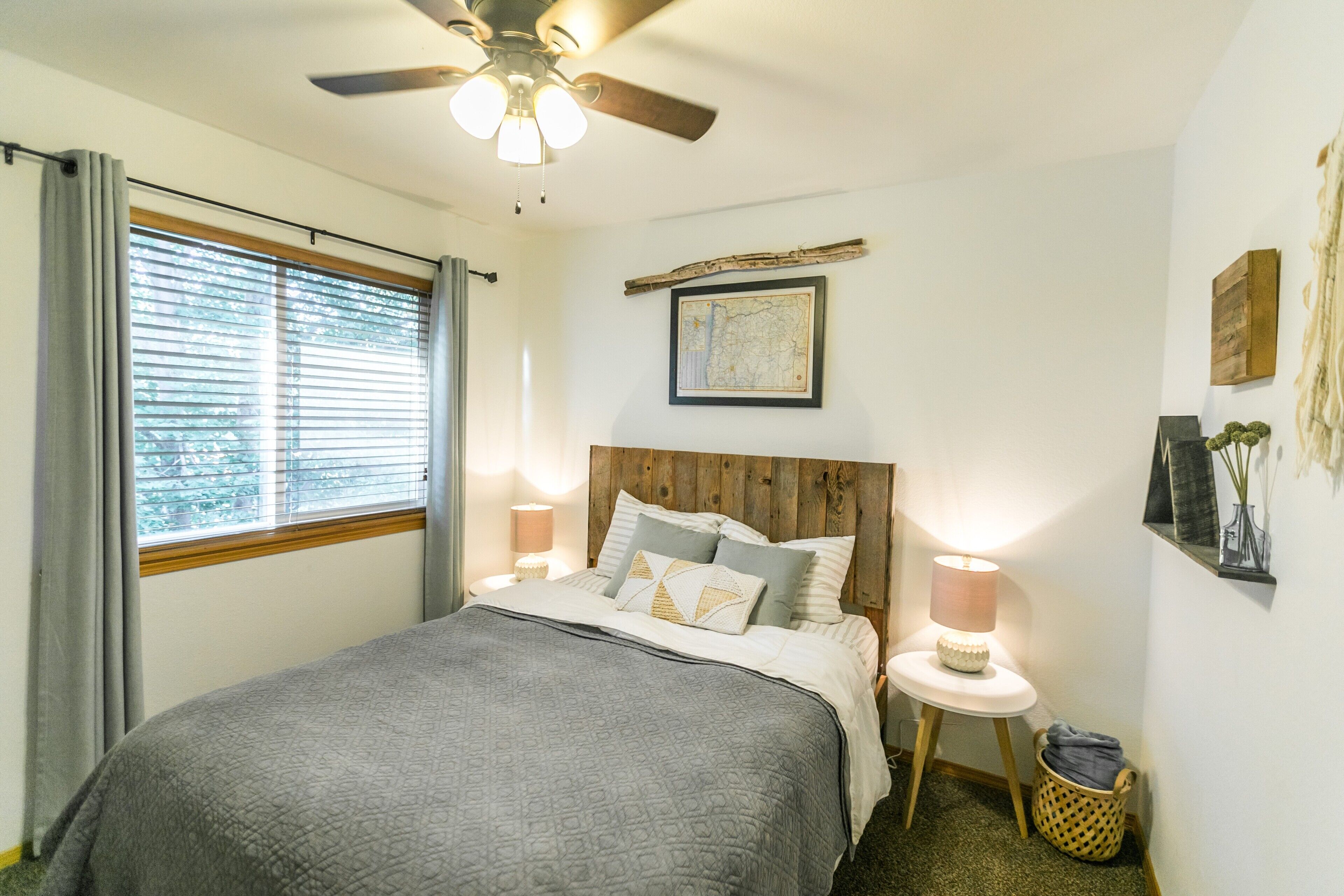 Ein Schlafzimmer mit Bett, Deckenventilator, Fenster mit Vorhängen, Nachttisch mit Lampe und einer an der Wand hängenden Karte.