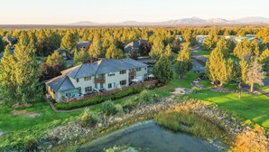 A residential area with a large house featuring a spacious backyard, a pond, and a view of distant mountains.