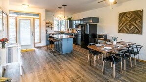 A modern kitchen with a central island, dark cabinetry, and a dining area with a wooden table and chairs.