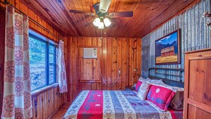 A wooden cabin bedroom with a bed, a ceiling fan, a window, and a painting on the wall. - Best View! Beautiful Ozarks cabin ON rim of AR Grand Canyon! Many new updates (Jasper)