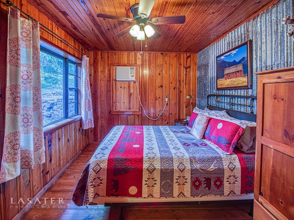 A wooden cabin bedroom with a bed, a ceiling fan, a window, and a painting on the wall. - Best View! Beautiful Ozarks cabin ON rim of AR Grand Canyon! Many new updates (Jasper)