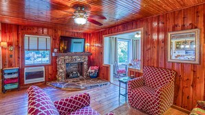 A cozy cabin interior with a stone fireplace, wooden walls, a ceiling fan, and a television. - Best View! Beautiful Ozarks cabin ON rim of AR Grand Canyon! Many new updates (Jasper)