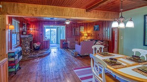 A cozy cabin interior with a stone fireplace, wooden floors, a dining area with a table and chairs, and a living room with a sofa and a patterned rug. - Best View! Beautiful Ozarks cabin ON rim of AR Grand Canyon! Many new updates (Jasper)
