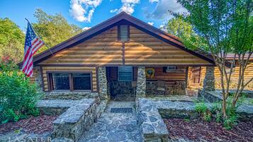A log cabin with a stone foundation, a flag, and a wreath on the front door.