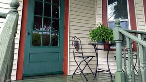 A porch with a green door, a small table with a potted plant, and a metal chair. - White Mountains Victorian on Main Street (Gorham)