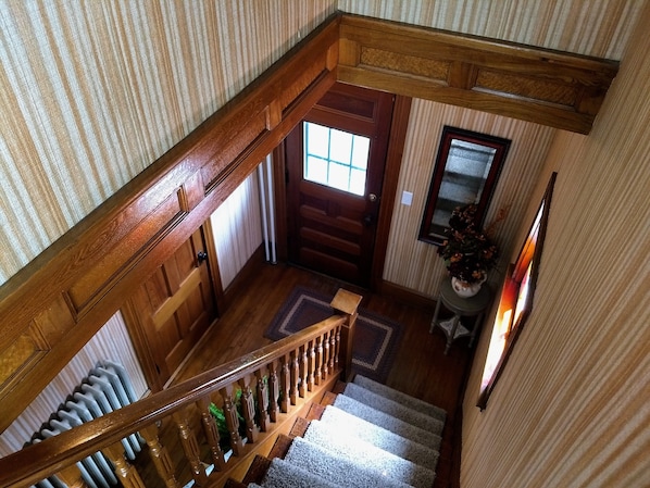 Un escalier en bois avec une rampe, une porte dotée d’une fenêtre et un petit tapis sur le palier.