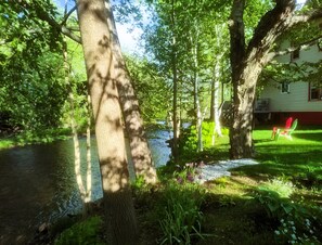 A riverside property with a house, trees, and a grassy area. - White Mountains Victorian on Main Street (Gorham)