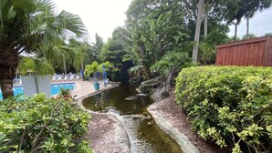 Un jardin paisible avec un petit étang, une végétation luxuriante et un espace piscine doté de chaises longues.