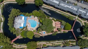 Vue aérienne d’un complexe hôtelier doté d’une grande piscine, d’un espace piscine séparé et d’un pont reliant les différentes parties de l’établissement.
