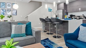 A modern living room with a grey sofa, blue armchair, and a kitchen area with grey cabinets and a white countertop. - Disney Getaway w/ Splash Pool + Kids’ Theme Rooms (Kissimmee)