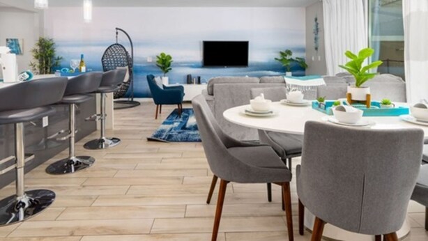 A modern living room with a round dining table, grey sofas, and a TV mounted on the wall. - Disney Getaway w/ Splash Pool + Kids’ Theme Rooms (Kissimmee)