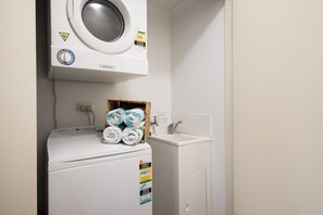 A compact laundry area with a washing machine, a dryer, and a small sink. - Waterlily - One Bedroom Apartment (Airlie Beach)