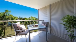 Un balcon avec une table et des chaises, une vue sur la verdure et une porte coulissante fermée.