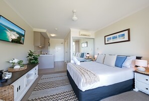 A bedroom with a large bed, a bedside table, a nightstand, a dresser, a mirror, and a wall-mounted TV. - Waterlily - Studio (Airlie Beach)