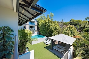 A modern outdoor pool area with a covered seating area and lush greenery. - Waterlily - Studio (Airlie Beach)