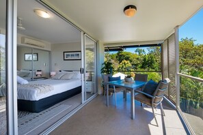 A modern bedroom with a glass door leading to a balcony, a dining area with a table and chairs, and a ceiling light fixture. - Waterlily - Studio (Airlie Beach)
