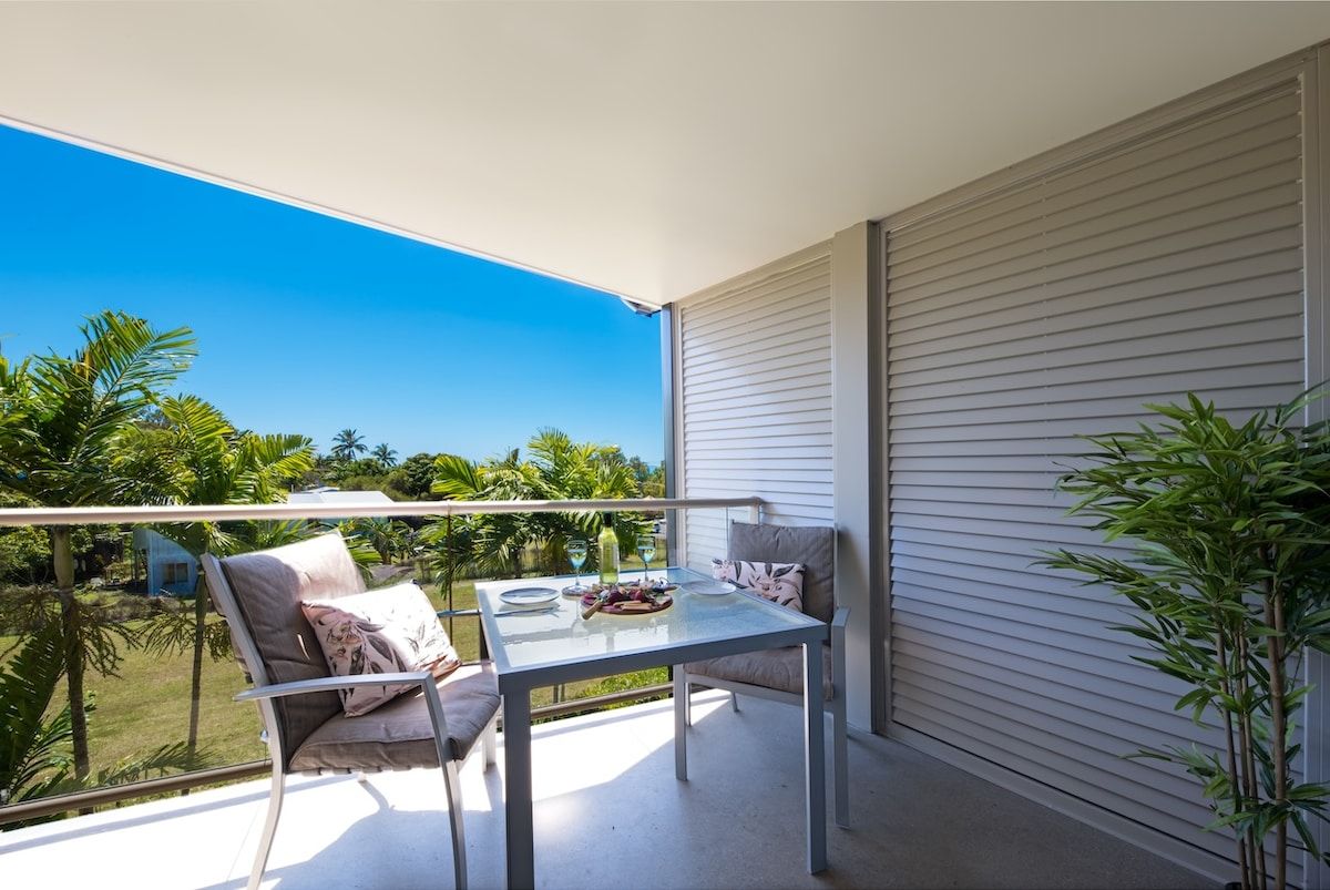 A balcony with a table and chairs, a view of greenery, and a closed sliding door.