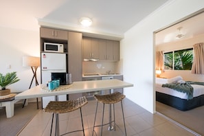 A compact kitchen with a microwave, refrigerator, and bar stools. - Waterlily - Two Bedroom Apartment (Airlie Beach)