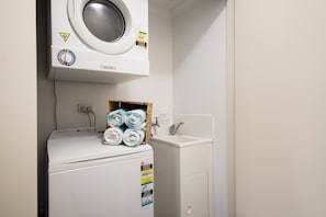 A compact laundry area with a washing machine, a dryer, and a small sink. - Waterlily - Two Bedroom Apartment (Airlie Beach)