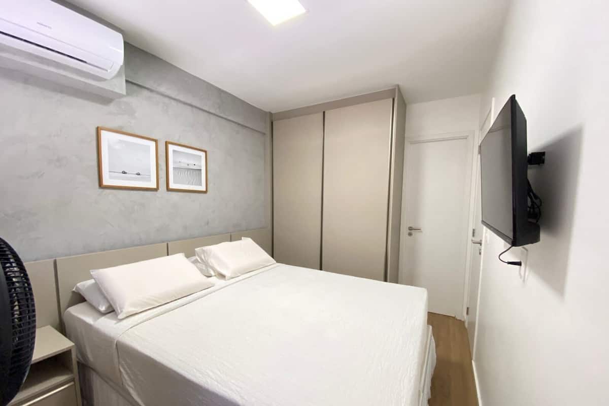 A hotel room with a bed, a TV, an air conditioner, and two framed pictures on the wall.