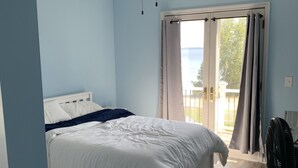 Quarto com cama, ventilador de teto, janela com cortinas e vista para o exterior.