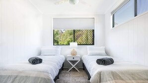 A room with two beds, a window with a view, a small table with a lamp, and a ceiling fan. - High On Jeffery in the Heart of Agnes Water (Agnes Water)