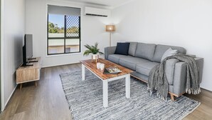 A modern living room with a grey sofa, a wooden coffee table, a floor lamp, and a large window. - High On Jeffery in the Heart of Agnes Water (Agnes Water)