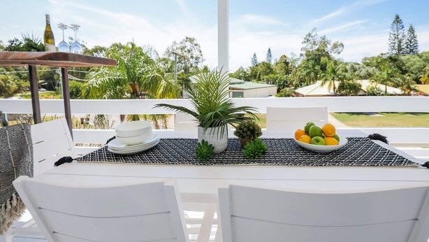 A table set with plates, a bowl of fruit, and a potted plant on a balcony with a view of trees and a building. - High On Jeffery in the Heart of Agnes Water (Agnes Water)
