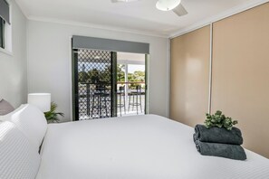 A bedroom with a large bed, a view of an outdoor seating area, and a sliding door to the balcony. - High On Jeffery in the Heart of Agnes Water (Agnes Water)