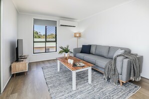 A modern living room with a grey sofa, a wooden coffee table, a floor lamp, and a large window. - High On Jeffery in the Heart of Agnes Water (Agnes Water)