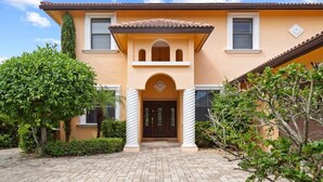 A two-story house with a tiled roof, a central entrance with a decorative arch, and a brick pathway leading to the door. - Pristine Waterfront Villa in Cape Coral with Lagoon Style Pool Spa and Boat Lift (Cape Coral)