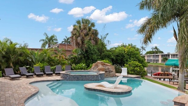 A swimming pool with lounge chairs, a hot tub, and a rock formation. - Pristine Waterfront Villa in Cape Coral with Lagoon Style Pool Spa and Boat Lift (Cape Coral)